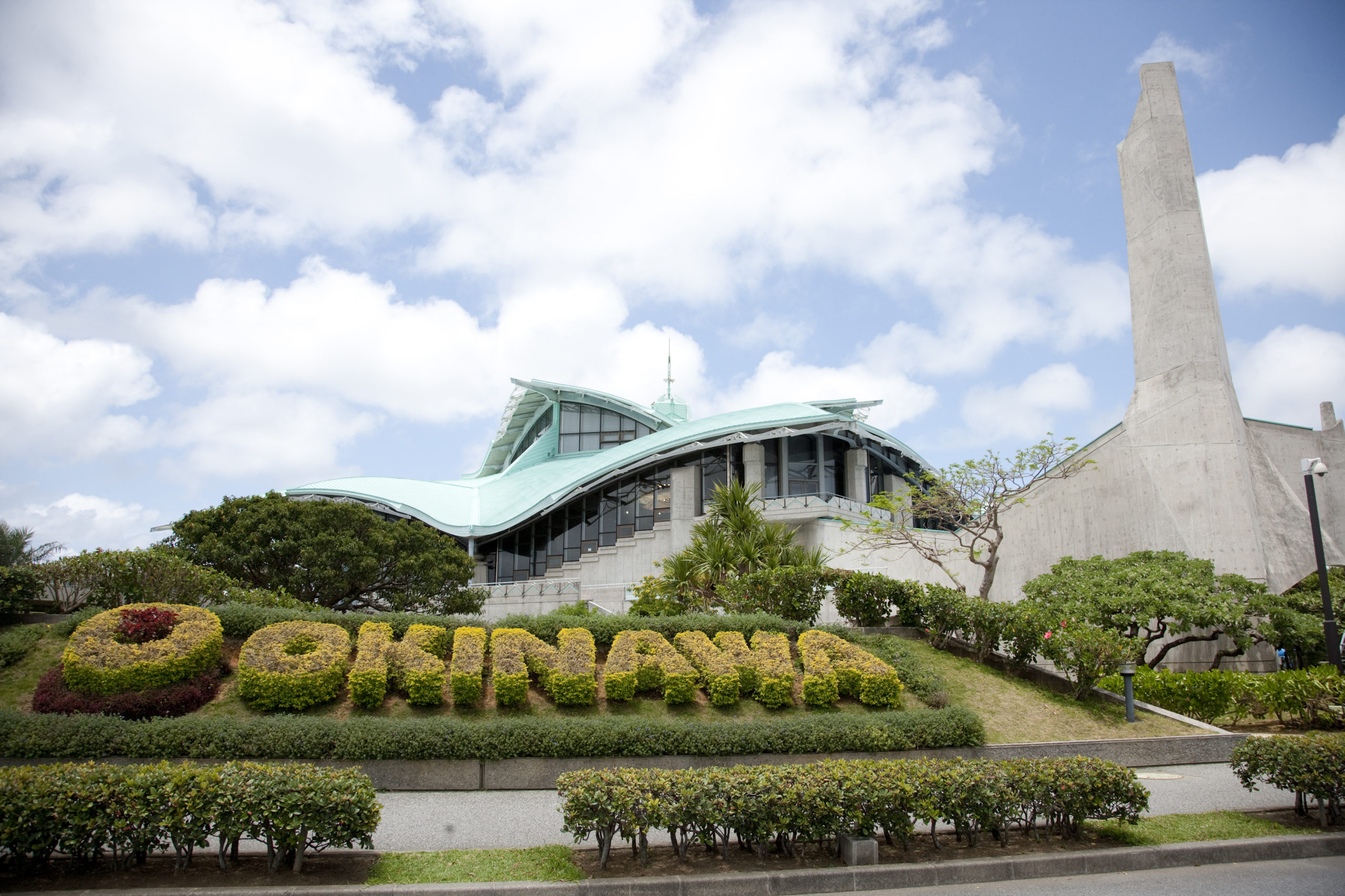 Exterior of the Okinawa Convention Center with the 'OKINAWA' topiary and the distinctive curved roof